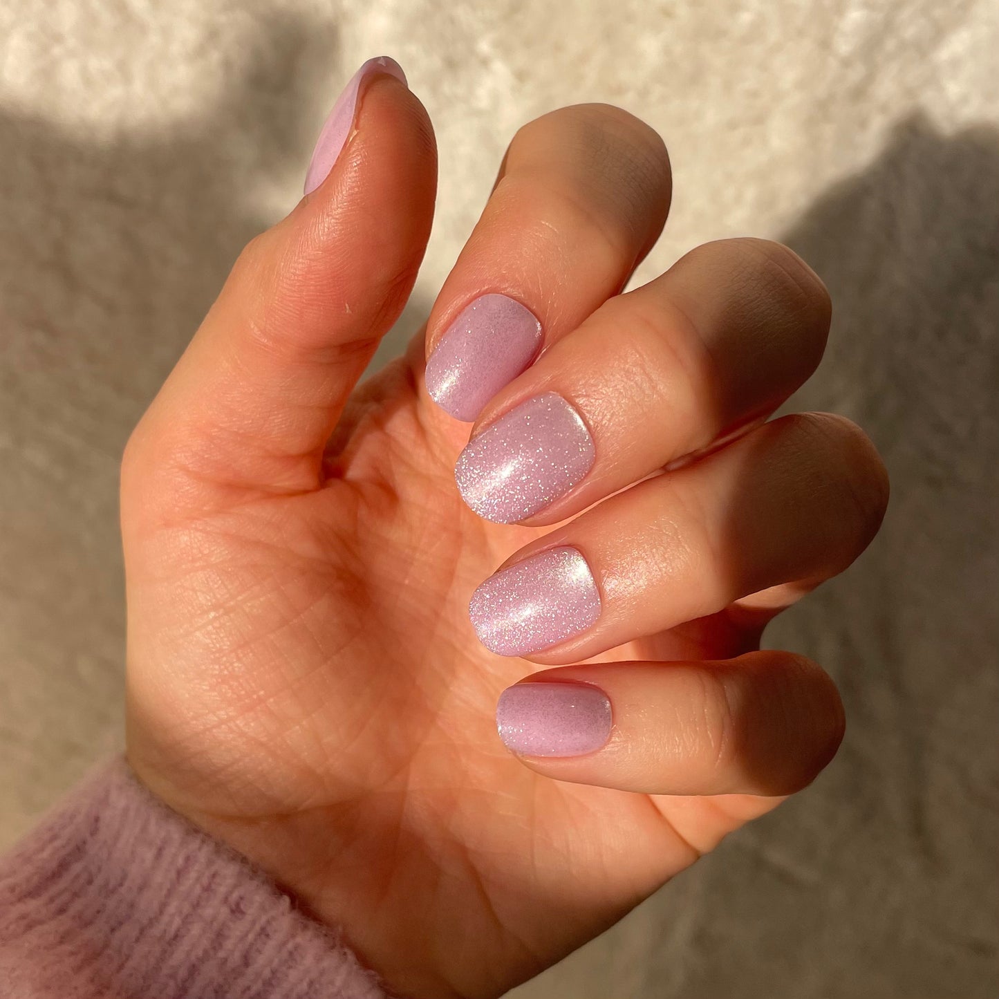 Woman's hand with Candy Claws false nails also called acrylic in shell shocked pink with pink jumper cuff