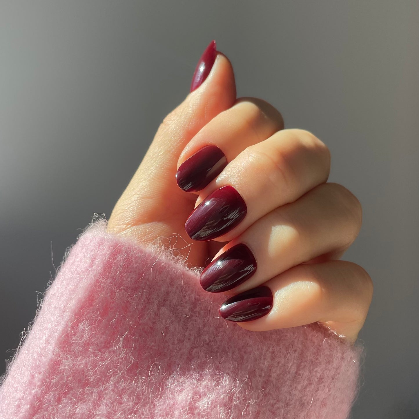 Womans hand wearing Candy Claws sour grape press-on false acrylic nails in short oval style. Rich deep plum colour