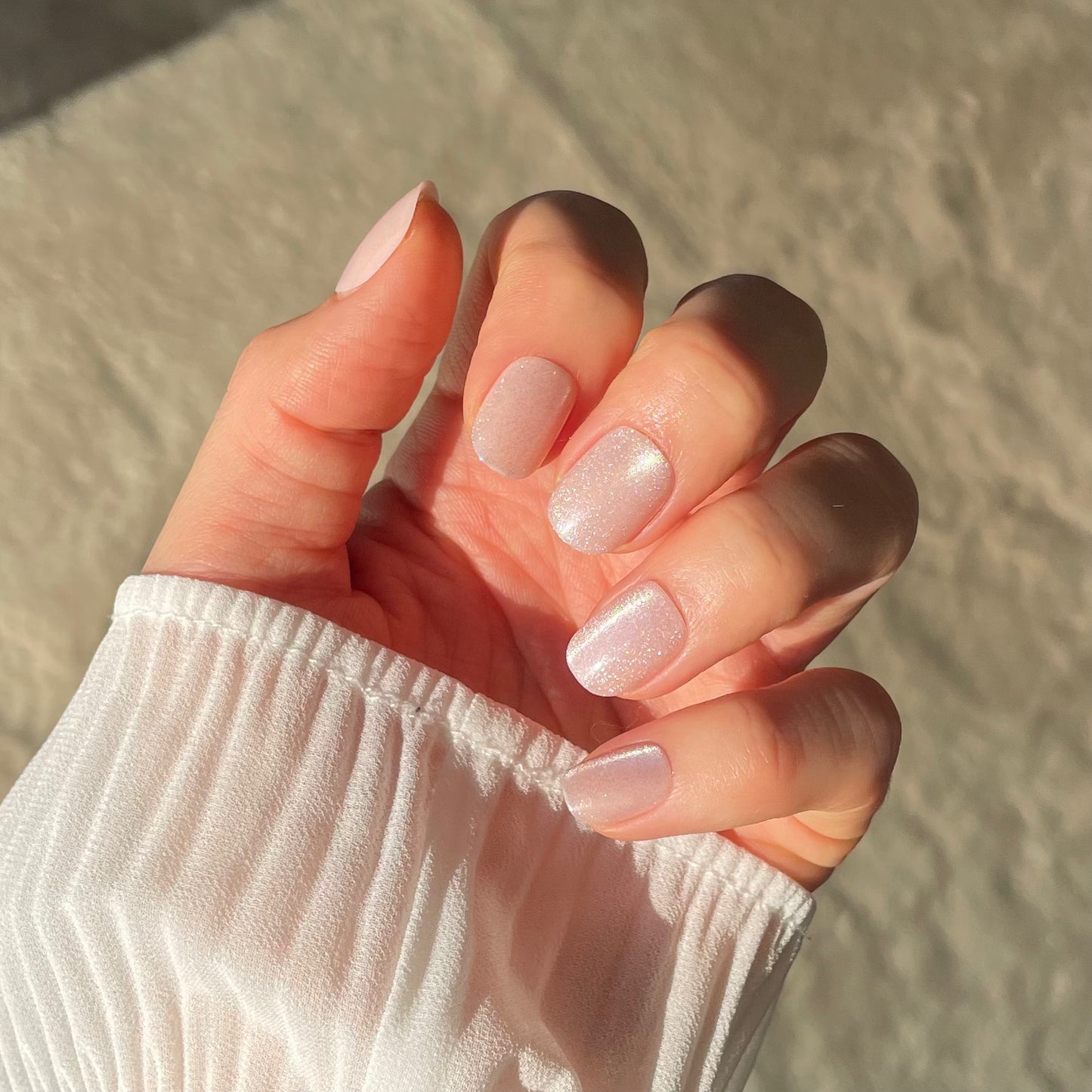 Womans hand showing pale pink glitter extra-short false nails from Candy Claws