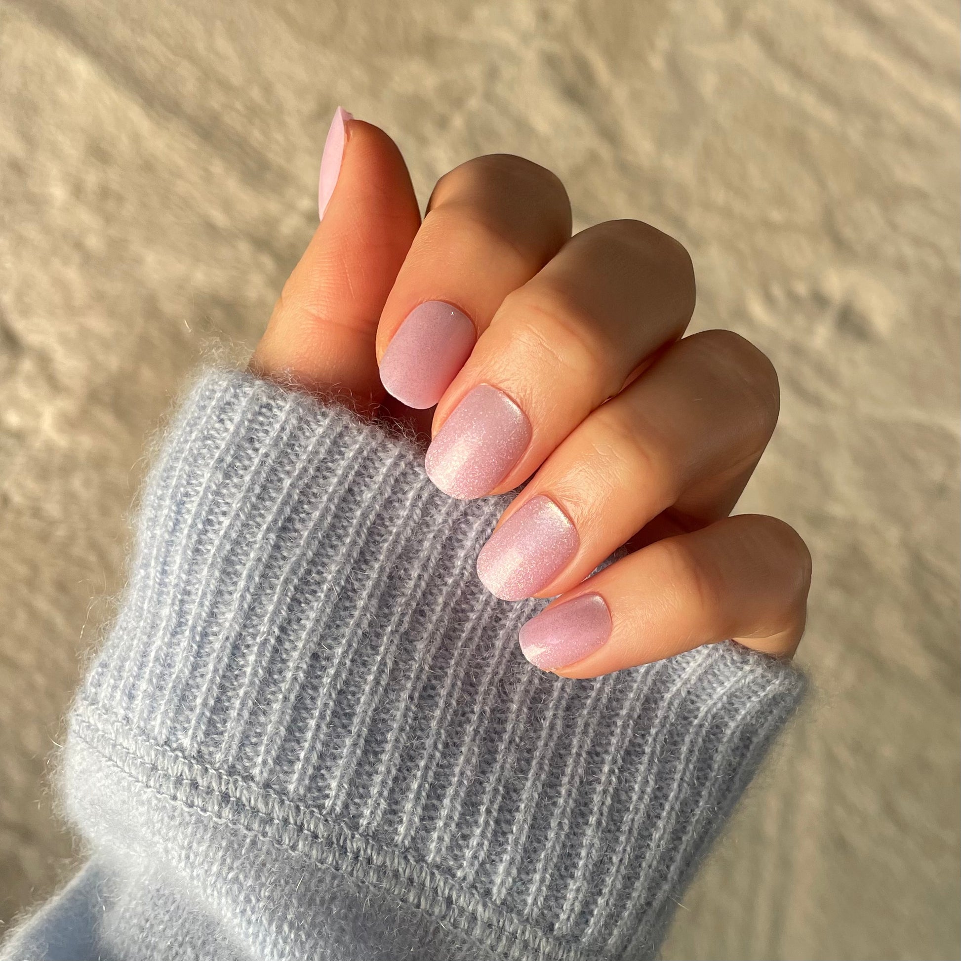 Woman's hand with blue jumper wearing Candy Claws shell shocked false nails, also called press-on or acrylic nails in shell shocked.