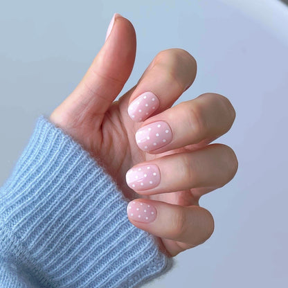 Womans hand with translucent pink press-on acrylic nails with white polka dots in the extra-short style